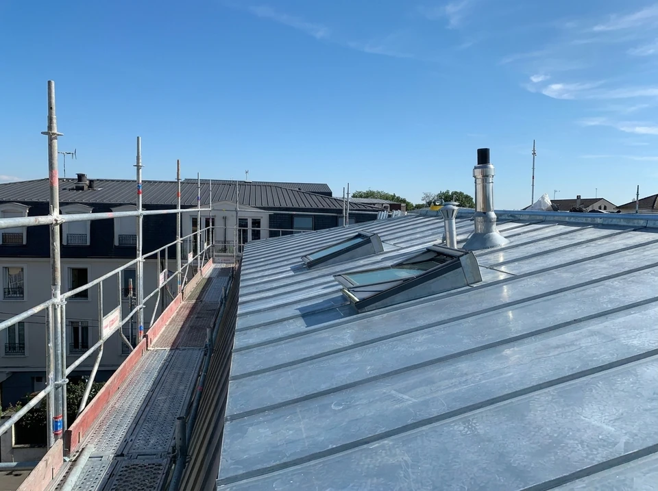 Ouvrier en combinaison bleue et harnais de sécurité rouge travaillant sur nacelle élévatrice jaune devant immeuble de bureaux moderne avec façade vitrée